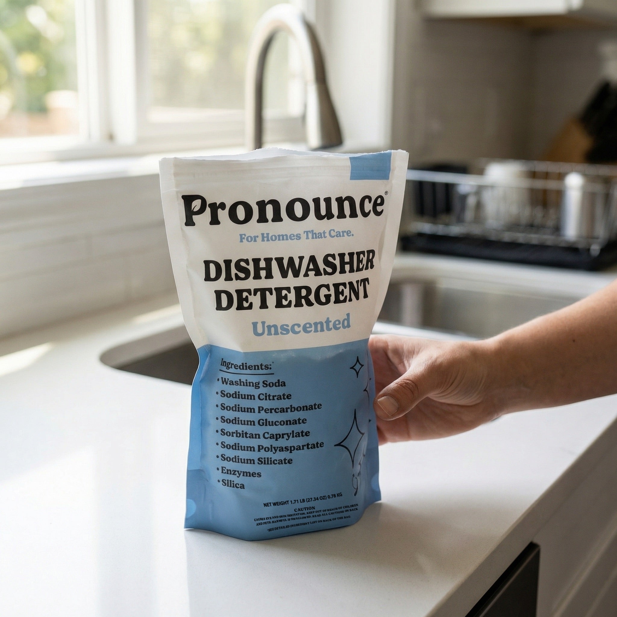Pronounce unscented dishwasher detergent pouch held at a kitchen sink